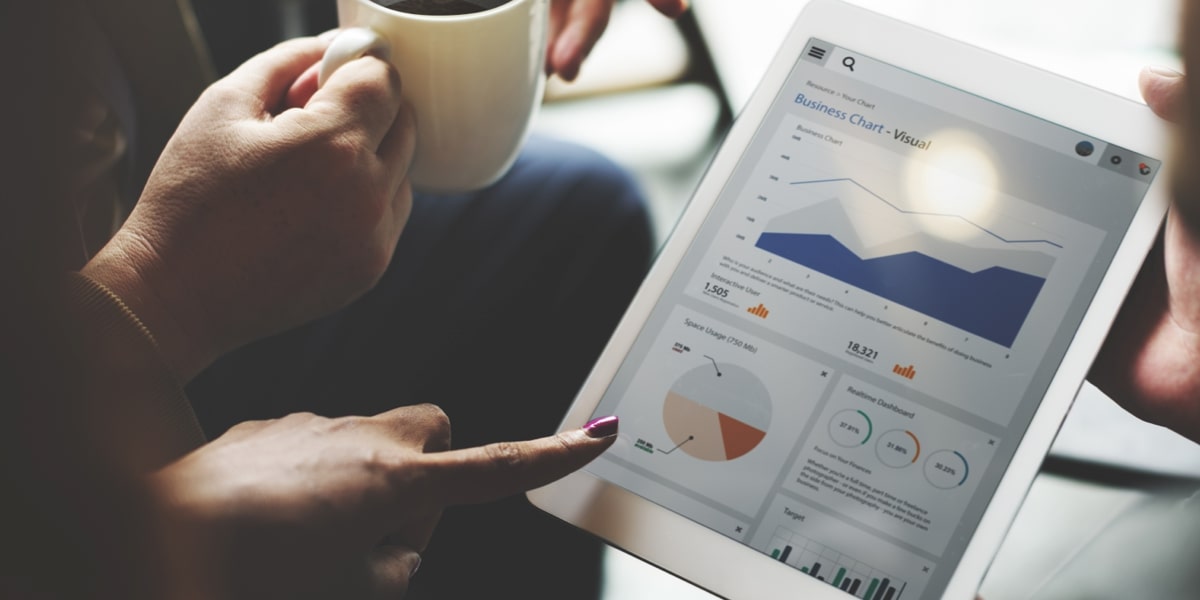 Person reviewing business analytics reports on a tablet while holding a coffee