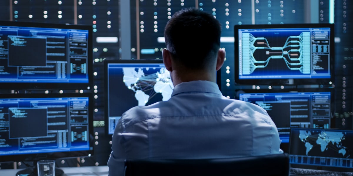 IT specialist monitoring global data systems on multiple screens in a control room