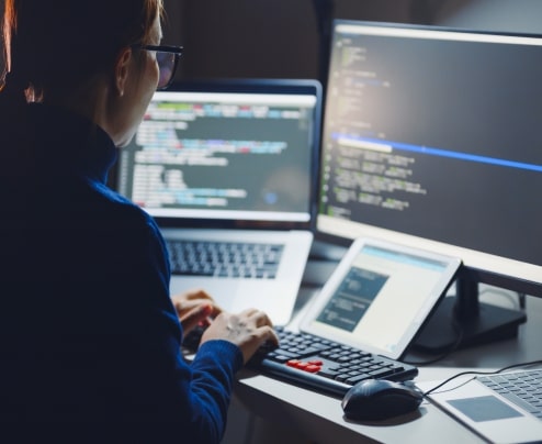 Developer working on a laptop with multiple screens displaying web application code