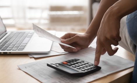 Person using calculator and laptop to manage financial data and online ERP billing tasks