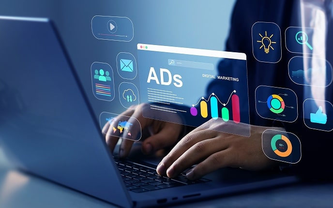 A person types on a laptop with floating digital graphics showing “ADs Digital Marketing,” colorful charts, and marketing icons like a lightbulb, graph, and user profiles, representing online advertising and data analysis.