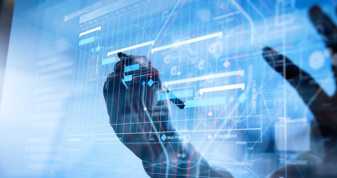 A hand holding a pen points to a transparent digital screen displaying a project management Gantt chart with tasks, timelines, and data charts in blue tones, suggesting planning or scheduling in a modern, tech-driven environment.