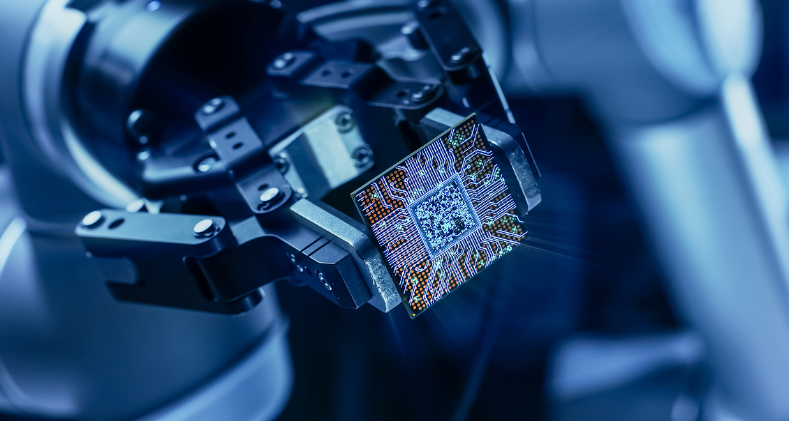 A robotic arm grips a complex microchip, positioned in bright blue light. The chip’s intricate circuits and patterns are clearly visible, highlighting advanced technology and precision engineering in a high-tech, futuristic environment.