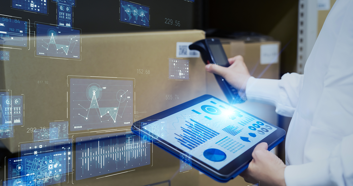 A person in a white coat scans a barcode on a cardboard box while holding a tablet displaying digital charts, graphs, and data analytics. Holographic interfaces and futuristic infographics are superimposed above brown packages in a warehouse setting.