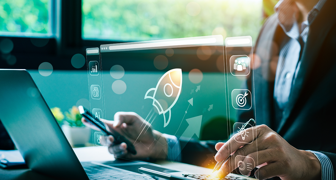 A person in business attire uses a stylus on a tablet and holds a smartphone. A laptop is nearby. Floating digital graphics show a rocket icon and various business symbols, suggesting startup growth or technological innovation in a modern office setting.