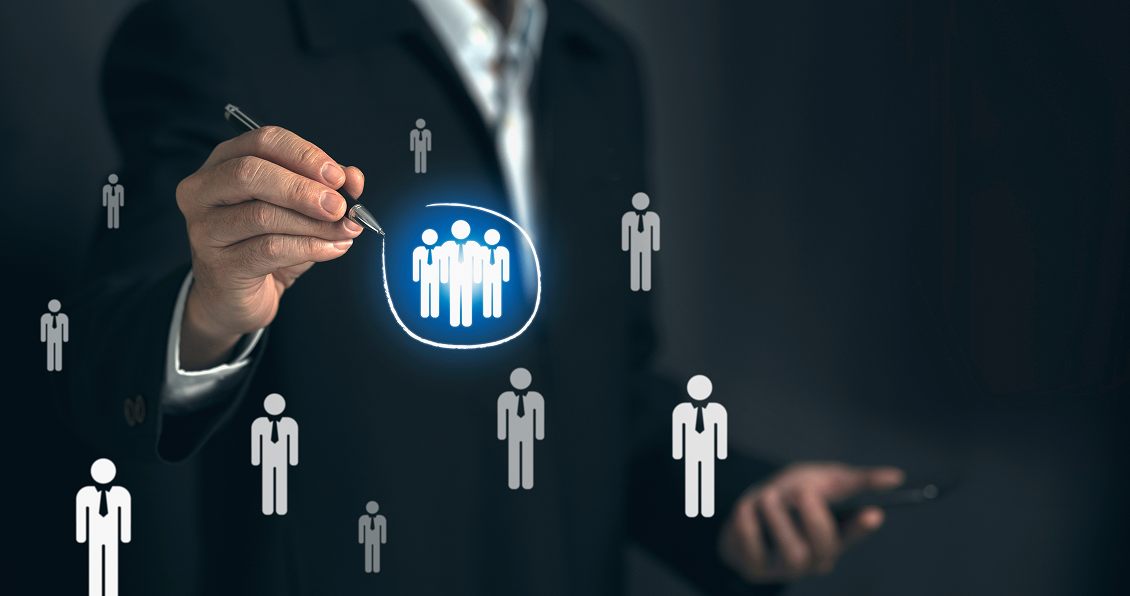 A person in a suit uses a pen to circle a glowing group icon among several human figure icons, representing targeting or selecting a specific group within a population, possibly for business, marketing, or recruitment purposes.