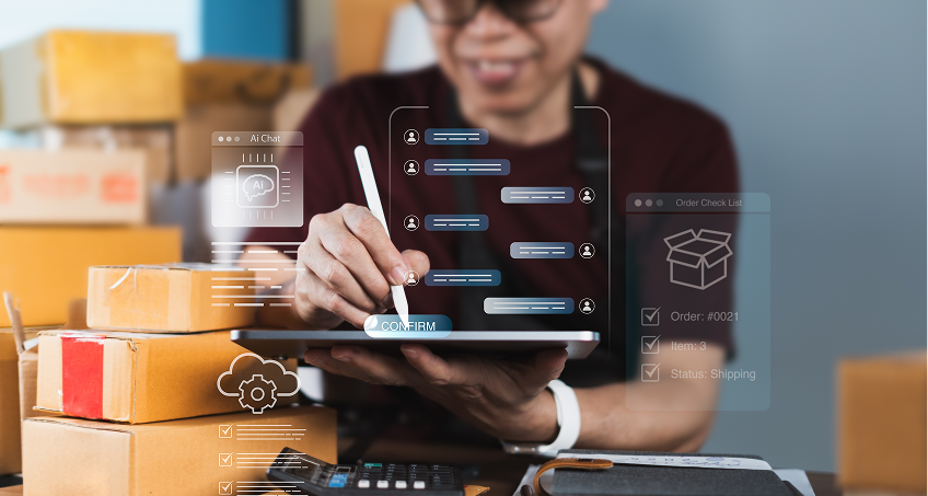 A person smiles while using a stylus on a tablet, surrounded by cardboard boxes. Digital graphics of chat bubbles and shipping icons appear over the image, suggesting online order management or e-commerce business activities.
