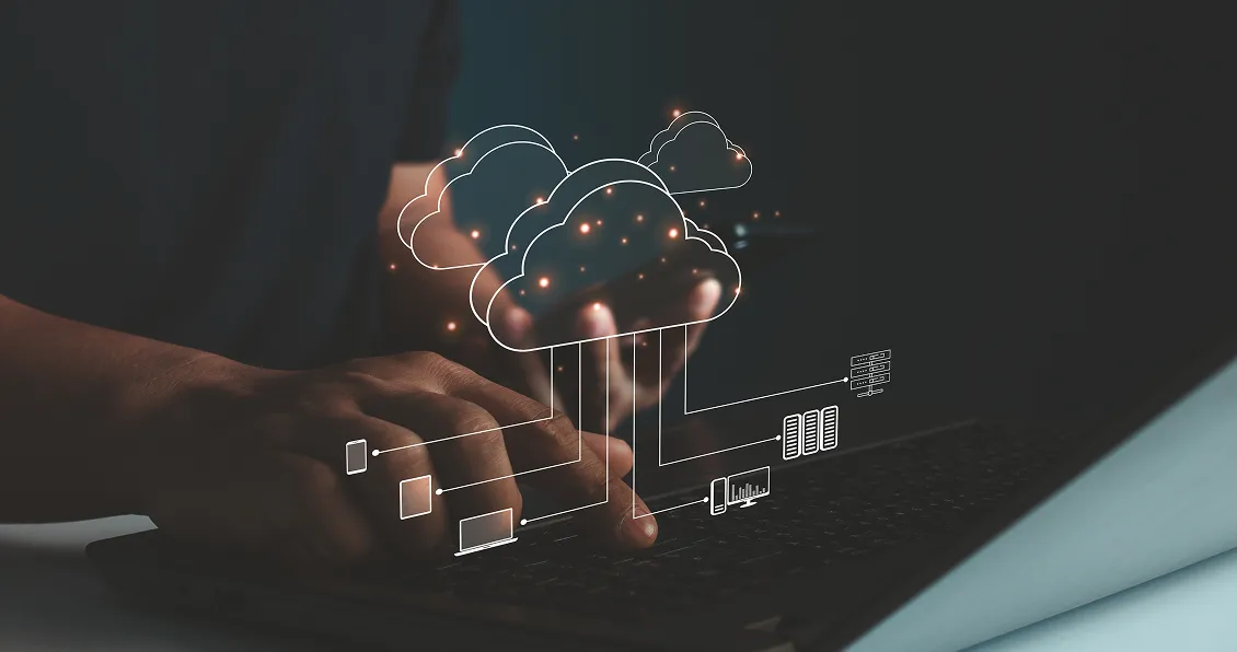 A person types on a laptop in a dark setting. A glowing, semi-transparent digital cloud icon with network connections and server graphics is superimposed above their hands, representing cloud computing and data storage technology.