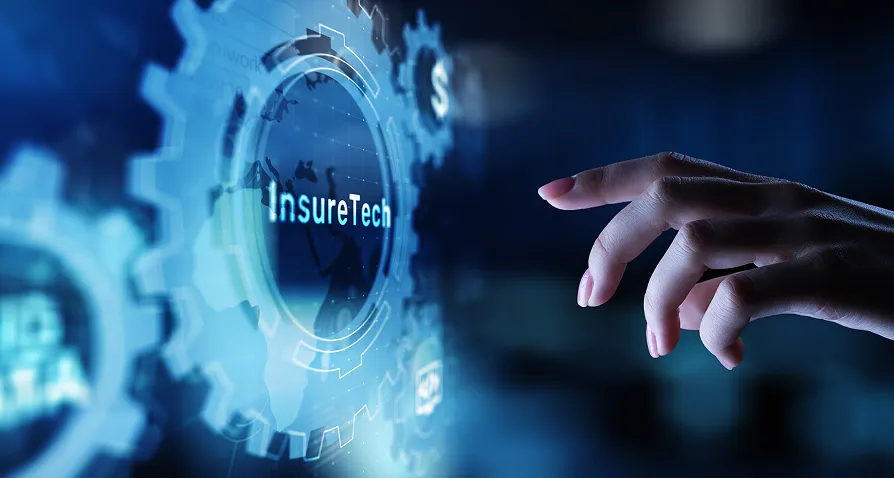 A hand reaches toward a transparent digital screen displaying blue gears and the word “InsureTech” in the center. The interface has a futuristic look, suggesting innovation in insurance technology, with faint data and tech graphics in the background.