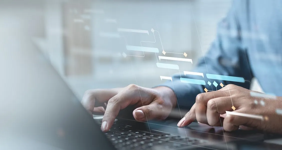 A person in a blue shirt uses a laptop, typing with both hands. Transparent digital charts and diagrams appear over the image, suggesting data analysis, project management, or technology-focused work in a modern professional setting.