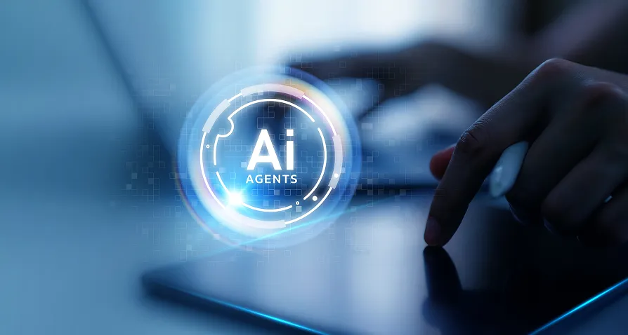 A hand uses a stylus on a tablet, with a glowing digital graphic overlay displaying the words “AI Agents.” A blurred laptop keyboard and blue-toned background emphasize the futuristic, tech-focused atmosphere.
