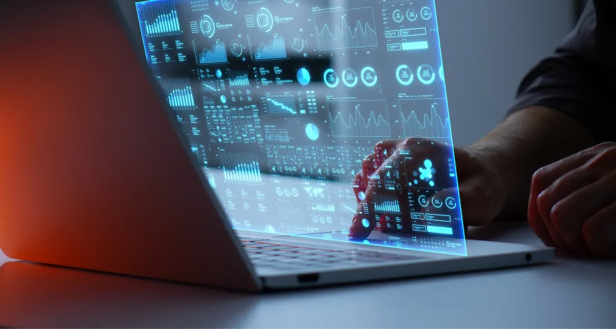 A person’s hands interact with a laptop displaying a holographic screen filled with blue data visualizations, charts, and infographics. The scene is futuristic, highlighting advanced technology and digital analytics, with the user analyzing or manipulating the data.