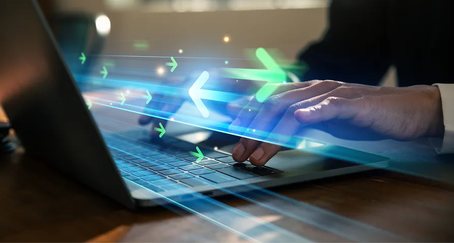 A person’s hands typing on a laptop keyboard, with glowing green arrows and blue light trails digitally superimposed, symbolizing speed, data transfer, or fast technology. The scene is set in a dimly lit indoor environment.