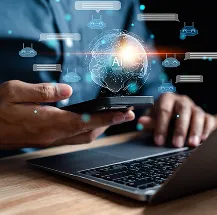 A person holds a smartphone above an open laptop. A glowing digital globe with AI in the center floats above the phone, surrounded by futuristic icons and chat bubbles, symbolizing artificial intelligence and technology integration.