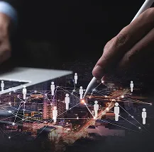 A hand holds a stylus near a laptop, overlaying a cityscape with white network lines connecting human icons, symbolizing digital communication and online networking. The image blends technology and urban life.
