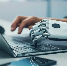 A close-up of a human hand and a robotic hand side by side, both typing on a laptop keyboard, symbolizing collaboration between humans and artificial intelligence or technology.