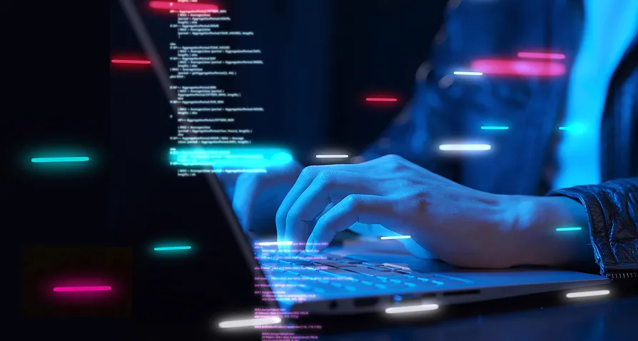 A person types on a laptop keyboard in a dark setting. Neon blue and pink light streaks and lines of computer code are superimposed on the image, suggesting programming, cybersecurity, or digital technology concepts.
